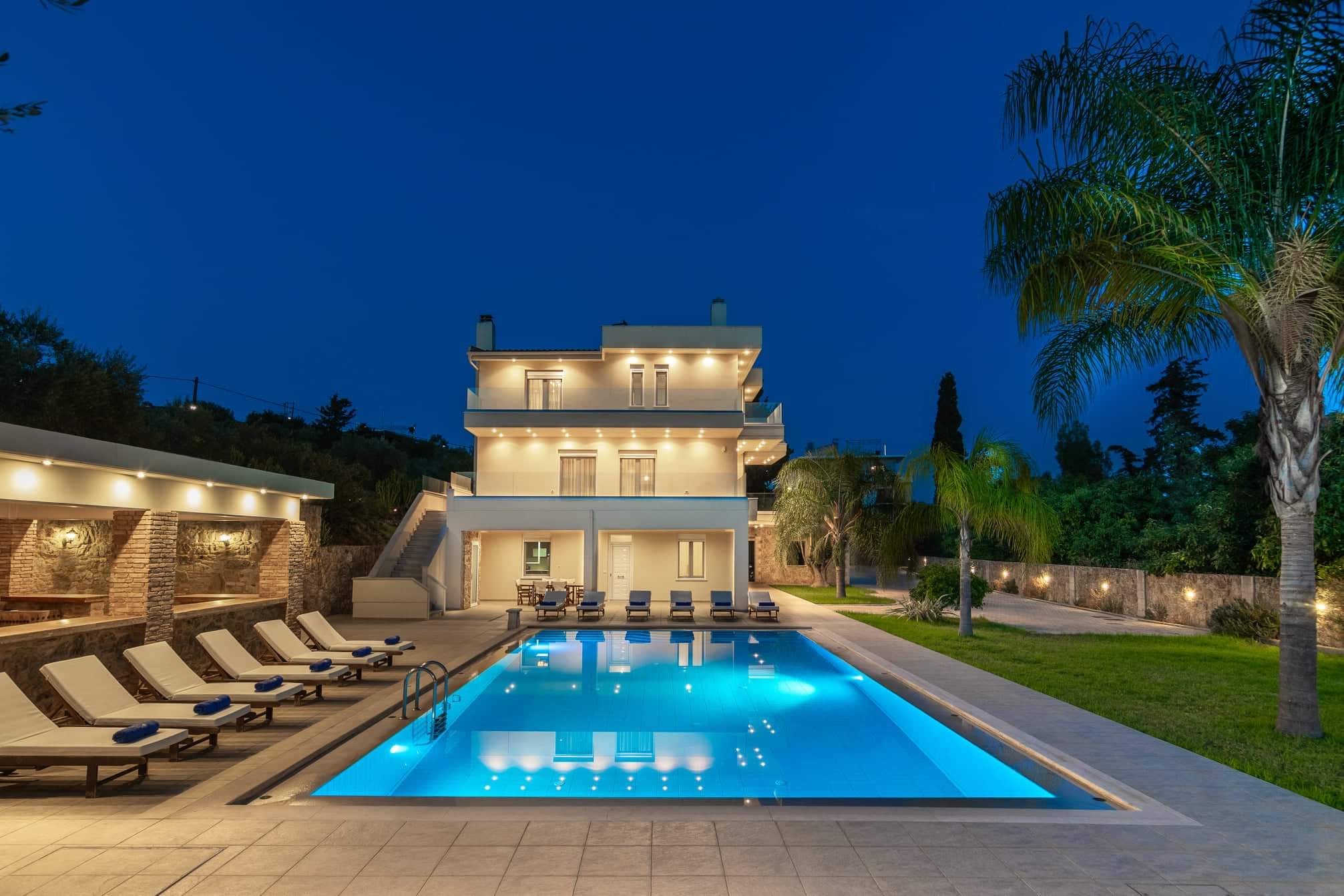 Villa Melitini at night — the illuminated three-level villa reflected in its glowing blue pool